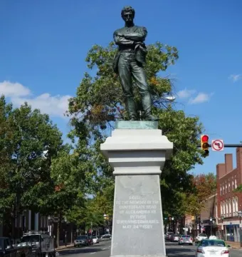Appomattox bronze statue of a man with crossed arms on a tall stone pedestal in a street