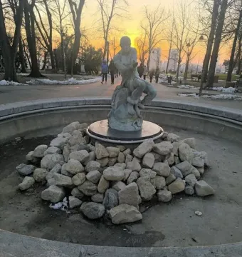 Fisherman Fountain statue in a park at sunset, with a man wrestling a snake in the center of a dry circular basin.