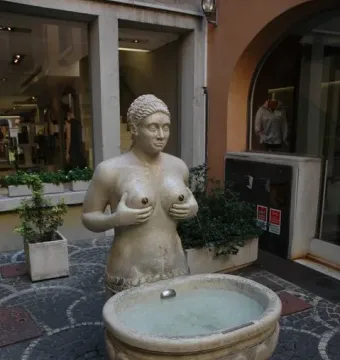 Fontana delle Tette stone fountain with a topless female bust and water flowing into a basin below.