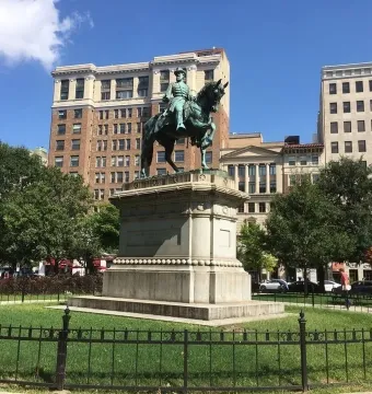Major General James B. McPherson Memorial equestrian statue on a tall pedestal in a grassy park with city buildings behind it.