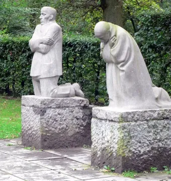 The Mourning Parents sculpture with two kneeling stone figures on separate pedestals outdoors.