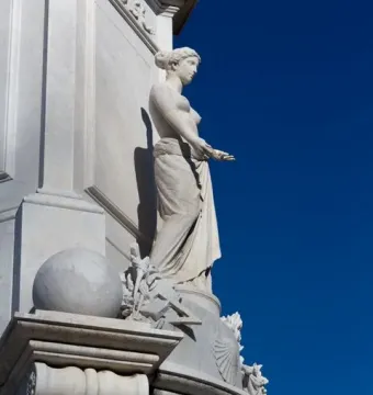 Peace Monument with a draped marble female figure and carved base against a blue sky.