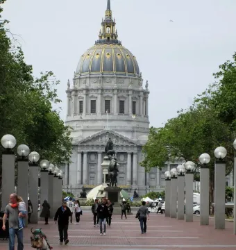 Pioneer Monument on a granite base in a brick-paved plaza, with San Francisco City Hall and its dome in the background.