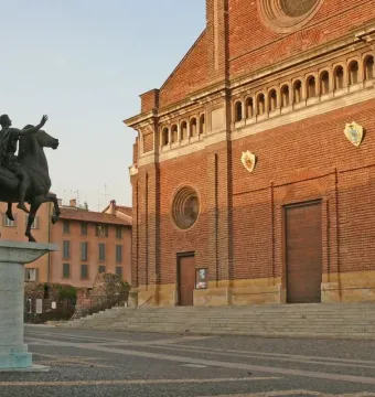 Regisole equestrian statue on a pedestal in a paved square with the cathedral of Pavia behind it.