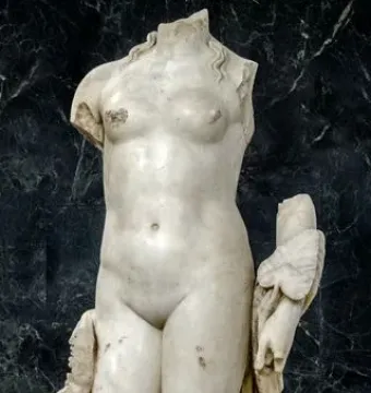 Headless marble sculpture of Venus Unica, with broken arms and draped fabric at the legs.