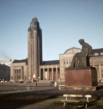 The Aleksis Kivi Memorial, a dark seated statue of a bowed man on a reddish-brown pedestal in a city plaza.