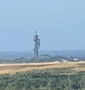 Birth of the New World sculpture silhouetted in the hazy distance above a bright landscape and water