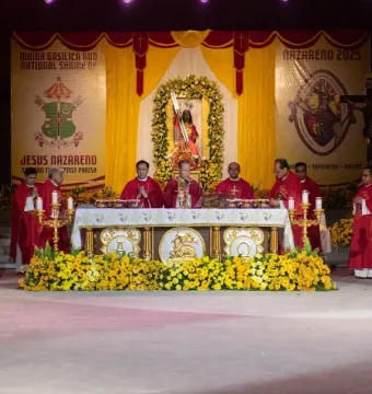 Black Nazarene statue in red and gold robes carrying a cross beneath a floral archway