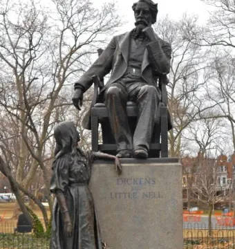 Bronze Dickens and Little Nell monument showing an author seated in an armchair with a young girl standing beside the pedestal.