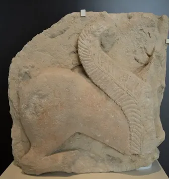 Weathered stone relief of the El Salobral Sphinxes shown in profile, with a large textured wing curving upward across the figure.