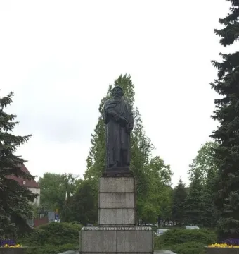 Mickiewicz Monument, a dark statue of a bearded man holding a book on a tall stone pedestal in a park.