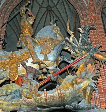Saint George and the Dragon sculpture showing a knight in golden armor on a grey horse battling a dragon inside a church