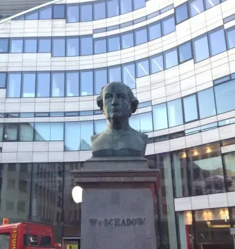 Schadow Monument with a bronze bust on a tall stone pillar and a modern curved building in the background.