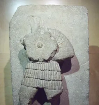 Stone relief from the Acrobat from Osuna showing a partial human torso with a ribbed skirt and the lower body in a dynamic pose.