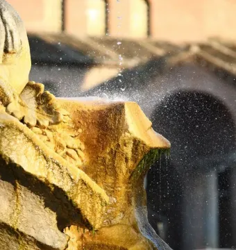 Weathered stone section of the Fountain of the Tritons with water spraying and dripping over green algae.