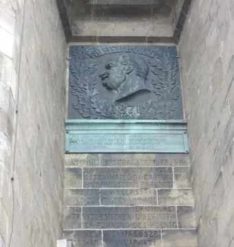 Bronze plaque on the Hermannsdenkmal showing a relief bust of a bearded man in profile, framed by a laurel wreath and the year 1871, with carved German inscription below.