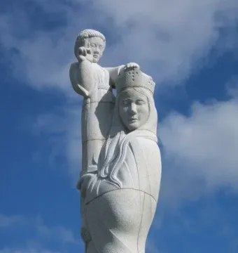 Detail of Our Lady of the Isles showing a crowned, veiled figure supporting a smaller figure against a blue sky.