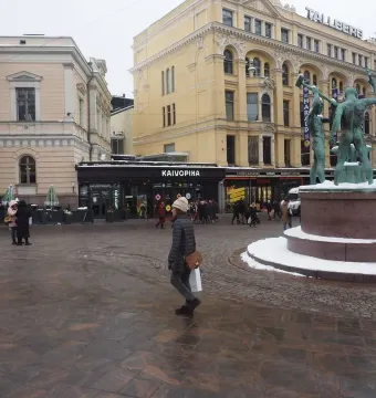 The Three Smiths sculpture on a snow-dusted pedestal in a busy Helsinki square.