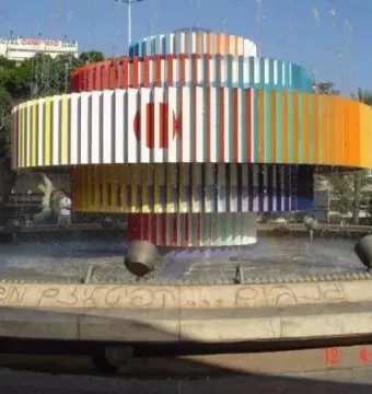 Fire and Water Fountain with colorful vertical slats spraying water into a circular basin, with a faint rainbow in the mist.