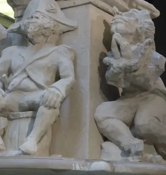 Two white figurative sculptures from Fons Americanus, one seated in a tricorn hat and formal jacket beside a kneeling figure with clasped hands.