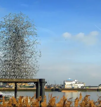 Quantum Cloud sculpture beside the water with buildings on the far shore under a clear sky.