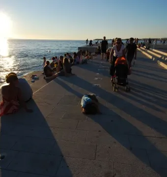 People gather along the Sea Organ promenade in Zadar at sunset, with dark circular openings visible in the stone steps by the sea.
