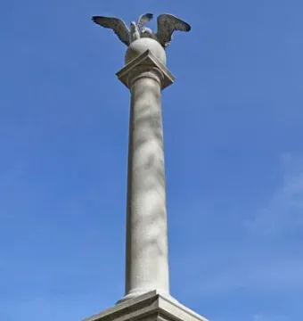 Seagull Monument with twin bird sculptures on a stone pedestal, framed by flowers against a blue sky.