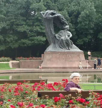 Chopin Monument in Warsaw surrounded by red roses, with people gathered around a reflecting pool.