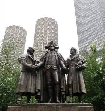 Heald Square Monument bronze sculpture of three historical figures on a red granite pedestal, with downtown skyscrapers behind it.