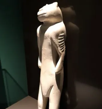 Lion-man sculpture with an animal-like head and slender human-shaped body, shown against a dark background.