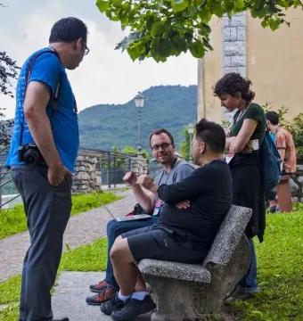 Five people gathered outdoors, with two seated on a stone bench and others standing nearby in conversation.