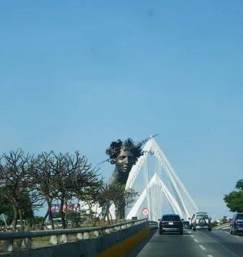 Reminiscencia, a dark bust of a woman with a spiky crown beside a white bridge structure.