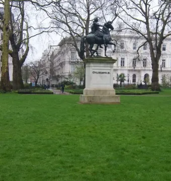 William III equestrian statue on a light-colored pedestal in a grassy park, with trees and buildings behind it.