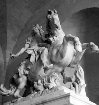 Equestrian Statue of Louis XIV shown as a marble rider on a rearing horse beneath a dark arched ceiling.