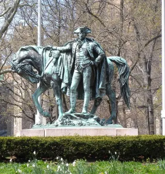 George Washington statue on a granite base with a horse beside it, framed by hedges and bare trees.