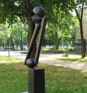 Große zwei V, a dark abstract metal sculpture with curved forms and upright beams on a base in a park setting.