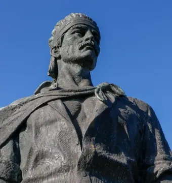 The Laçador bronze statue shows a man with a mustache and headband looking upward against a blue sky.