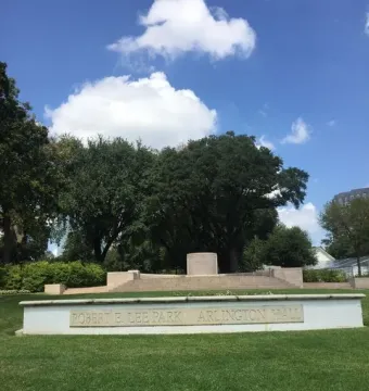 Stone marker for Robert E. Lee Park Arlington Hall in front of an empty stone platform on a grassy lawn.