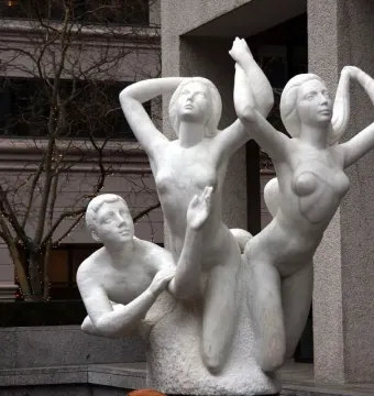 The Quest sculpture showing three marble nude figures outdoors, with a kneeling male figure and two women reaching upward.