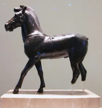 Bronze horse sculpture standing on a pedestal, facing left with clear support rods under the rear legs.