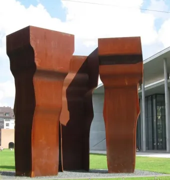 Buscando la Luz II sculpture with three tall rust-patinated metal forms on a grassy lawn.