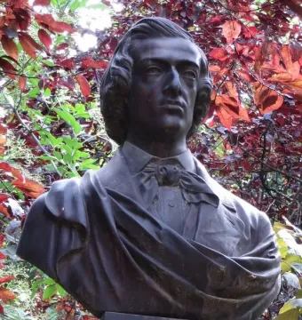 Frederic Chopin bust on a stone base, set against foliage with red and green leaves.