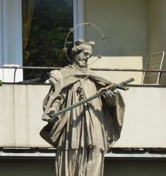 Stone statue of Saint John of Nepomuk holding a crucifix and palm frond, with a halo of stars.