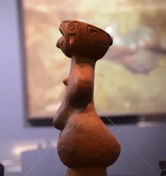 Jōmon Venus clay figurine shown in profile on a dark display surface.