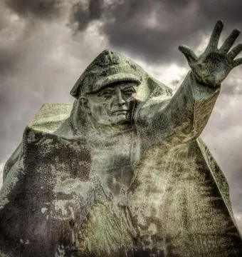 Kościuszkowców Memorial bronze figure with raised hand against a cloudy sky