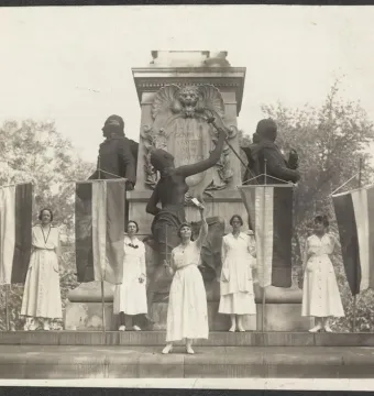 Seven women stand on the steps of the Marquis de Lafayette statue, holding banners beside the monument.