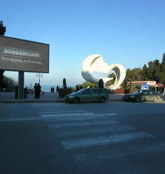 Peace Dove, a large white bird-like sculpture with spread wings in a park beside a street.