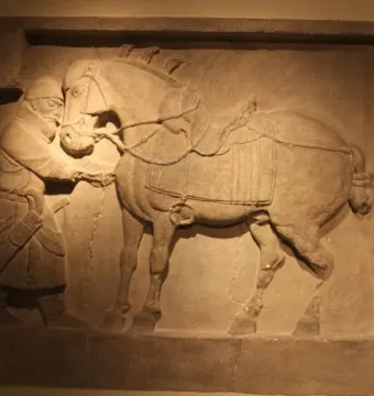 Stone relief of a saddled horse attended by a helmeted figure from the Six Steeds of Zhao Mausoleum.