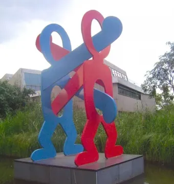 The Boxers sculpture by Keith Haring with two intertwined figures in blue and red on a platform in a pond.