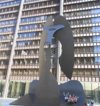 The Picasso abstract sculpture in a plaza beside a tall windowed building, with people gathered around its base.